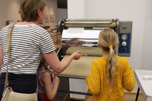 Mutter mit Kind vor einer Druckerpresse. Foto: Horst-Janssen-Museum