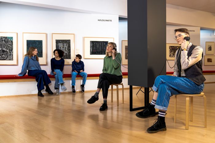 Besuchende hören sich einen Info-Film über Drucktechniken an. Foto: Studio 3x3